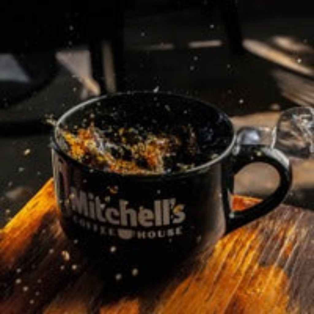 Black mug with 'Mitchell's Coffee House' branding on a wooden surface.